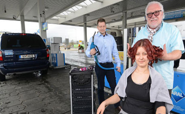 Proprietário de posto de gasolina oferece serviços de cabeleireiro enquanto clientes abastecem seus carros.