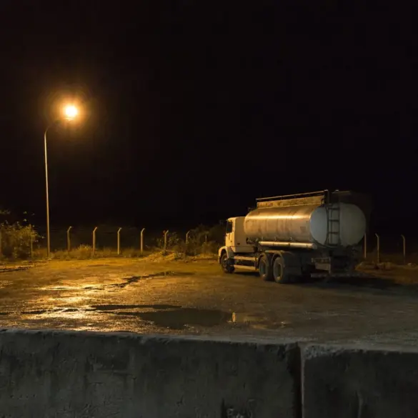 Caminhão-tanque estacionado à noite em pátio iluminado por um poste, com cerca ao fundo